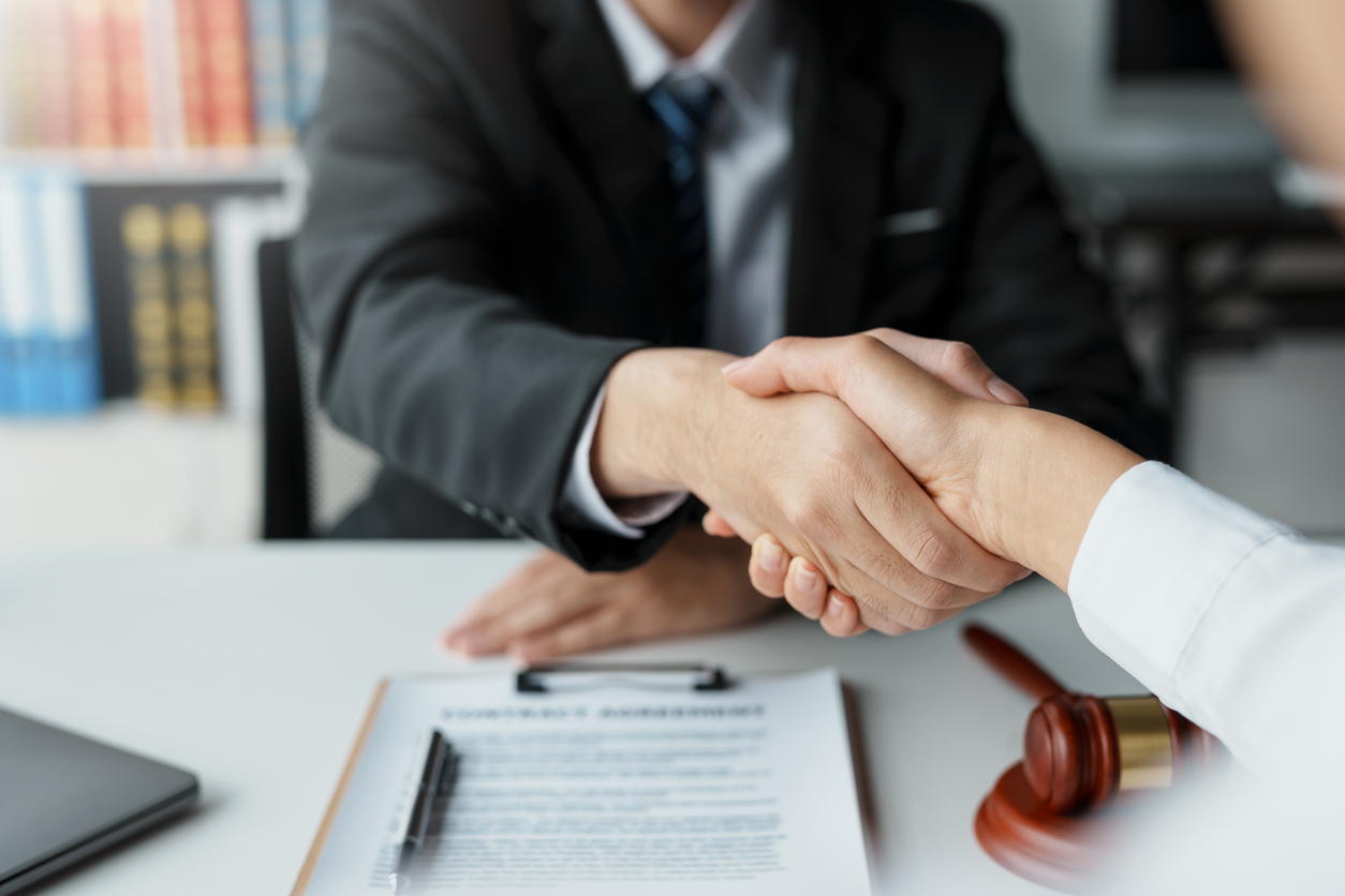 Lawyer shaking hands with a client making about documents, contracts, agreements, cooperation agreements with a female client at the lawyer's desk and a hammer at the table.
